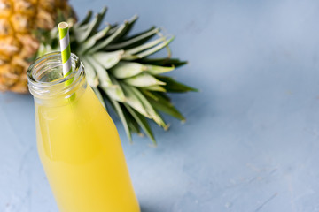 Tasty Pineapple Cocktail or Juice in Glass Bottle with Straw and Pineapple on a Blue Background Copy Space