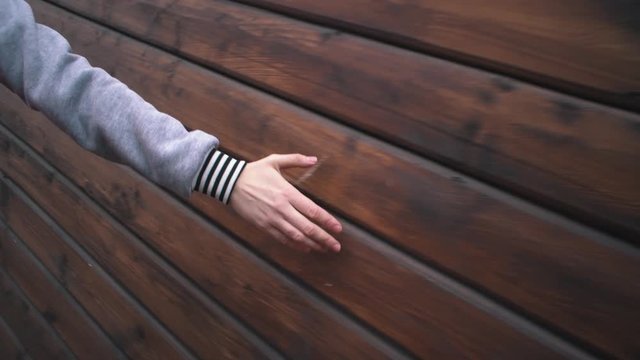 Handheld shoot close up female hand touches hard rough woody wall on cloudy day. Human runs his hand along brown boards on wooden surface.