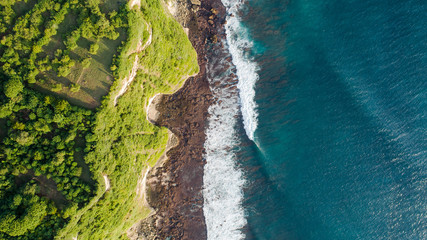 Sharp aerial top down of cliff and waves crushing into rocks in Uluwatu, Bali, Indonesia – Green and blue vibrant colours – Natural wonder – Drone Image