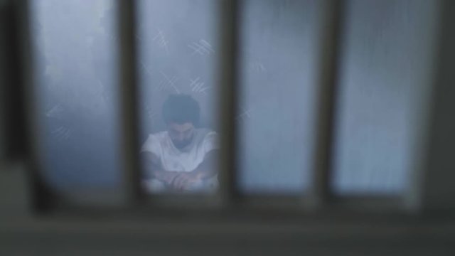 A sad oppressed young man sitting in prison dark room