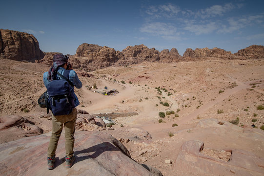 Asian man traveler and photographer taking photo of rock desert landscape in Petra, Jordan from scenic viewpoint. Travel Middle East concept