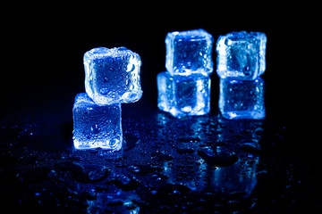 Blue ice cubes reflection on black table background.