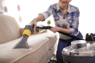 Fototapeta na wymiar Woman removing dirt from sofa with vacuum cleaner at home, closeup