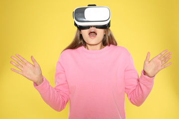 Emotional young woman playing video games with virtual reality headset on color background