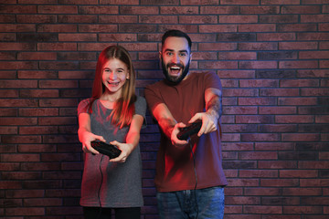 Young man and teenage girl playing video games with controllers near brick wall © New Africa