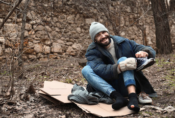 Poor homeless man sitting on cardboard in city park