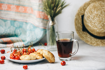 healthy light breakfast. sweet cherry with croissants on a plate. bouquet in a vase with spikelets of wheat. tea in a cup. Straw hat. proper nutrition for a slim figure. raw foods vegetarianism. diet