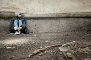 Poor homeless man sitting near wall on street. Space for text
