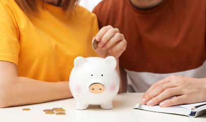 Obraz na płótnie Canvas Couple putting coin into piggy bank at table, closeup. Saving money