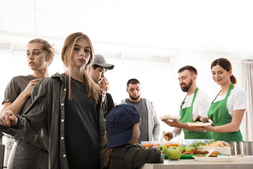 Teenage girl with other poor people receiving food from volunteers indoors