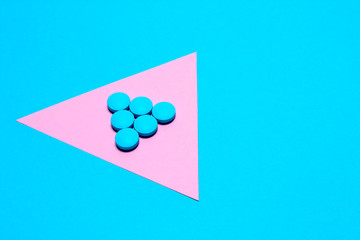 blue tablets laid out in the form of a triangle or an arrow on a paper background of blue and pink with copy space