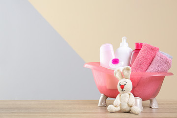 Baby cosmetic products, knitted rabbit and towels on table against color background. Space for text