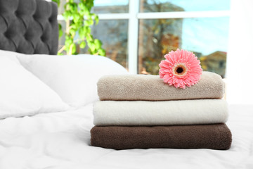 Obraz na płótnie Canvas Stack of clean towels and beautiful gerbera flower on bed. Space for text