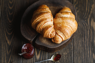 Freshly baked croissants with jam on wooden rustic background. Tasty croissants