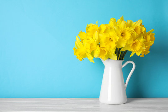 Bouquet of daffodils in jug on table against color background, space for text. Fresh spring flowers