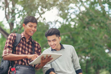 Study concept.Asian Students reading book,studying for an exam at university.Happy multi ethnic friend successfully completes the thesis report in park.