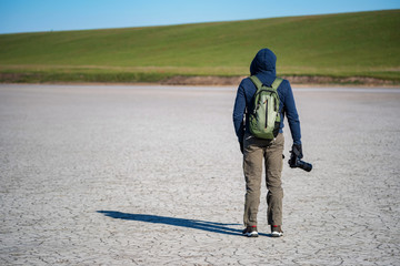 Young man with camera in steppe in spring on dry soil