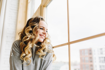 Fototapeta premium Beautiful young caucasian European woman sitting on windowsill looking out of the window