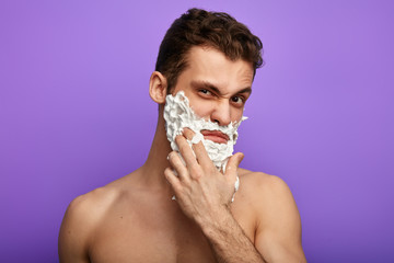 frustrated man with face covered with shaving foam hates shaving process. close up photo. isolated in the blue background.