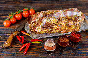 Raw uncooked rack of lamb on wooden chopping board with salt, pepper and dry herbs over old wood background.