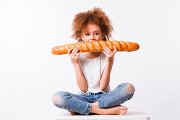 Curly mom and daughter eat big baguette on a light background.
