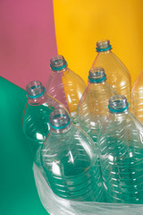 A pack of 7 empty and recyclable plastic water bottles, with no caps, blue seal, in a plastic bag, on a colored pastel tones of sea green, soft pink and yellow background. Reuse, Eco-Friendly