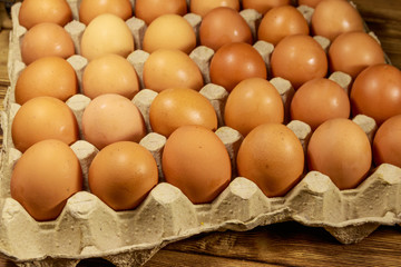 Raw chicken eggs in cardboard pack on wooden table