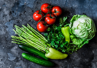 Fresh vegetables - tomatoes, asparagus, cabbage, cucumbers, peppers and cilantro on a dark background, top view. Healthy food diet concept. Flat lay