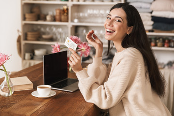 Photo of beautiful brunette woman 20s using laptop computer in kitchen at home