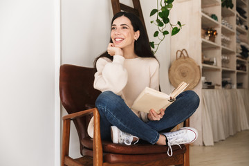 Photo of young lovely woman 20s reading book while sitting on chair