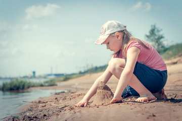 Cute young girl having fun on a sandy lake beach on warm and sunny summer day. Young girl playing by the river. Summer activities for children.