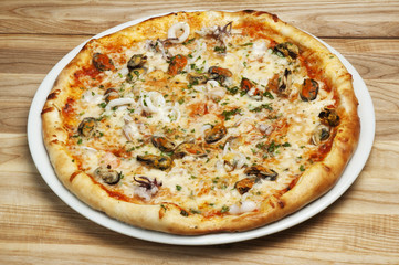 Delicious pizza with cheese, mushrooms and seafood on a wood background