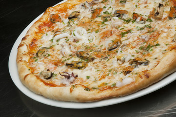 Delicious pizza with cheese, mushrooms and seafood on a black background