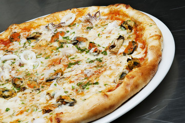 Delicious pizza with cheese, mushrooms and seafood on a black background