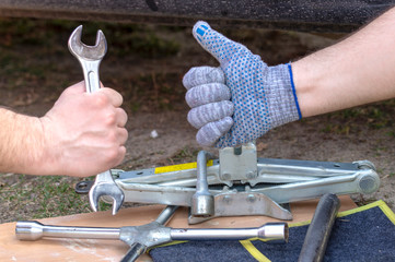 Two hands mechanics close-up. One holds a wrench and the other shows the OK sign