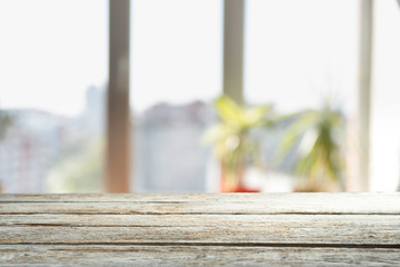 Wood table top on blur of window glass and abstract green from garden with city view in the morning background. For montage product display