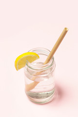 Fototapeta na wymiar Bamboo straw in a glass of lemon water on the pink background, Reusable bamboo straws as an alternative for single-use plastic straws, healthy and sustainable lifestyle concept