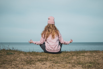 Young adult woman in pink hat sitting alone on the bluffs, looking of sea, freedom concept,...