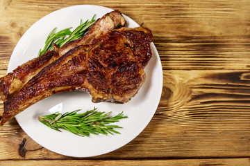 Roasted beef rib eye steak on bone with rosemary in white plate on wooden table
