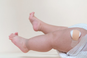 baby boy legs with a band-aid patch after taking a vaccine. doctor or nurse putting plaster on baby leg at the hospital.