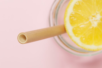 Bamboo straw in a glass of lemon water on the pink background, Reusable bamboo straws as an alternative for single-use plastic straws, healthy and sustainable lifestyle concept
