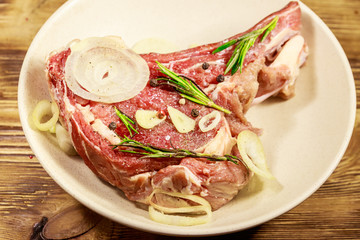 Marinated beef rib eye steak on bone with spices, onion and rosemary on wooden table