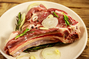 Marinated beef rib eye steak on bone with spices, onion and rosemary on wooden table
