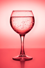 Wine glass with liquid (white wine) on a red background