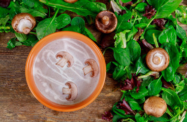 Cream soup of mushrooms with a purple bowl on a dark wooden table.