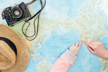 Cropped view of child and woman with film camera and straw hat pointing with fingers on world map