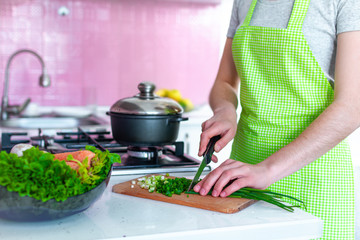 Woman in apron standing near stove and chopping vegetables on cutting board for soup at kitchen. Cooking preparation for dinner. Clean healthy food and proper nutrition.