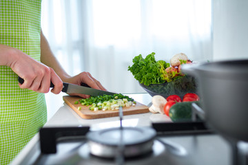 Woman in apron chopped vegetables on chopping board for vegetables dishes and fresh salads at kitchen at home. Cooking preparation for dinner. Clean healthy food and proper nutrition.