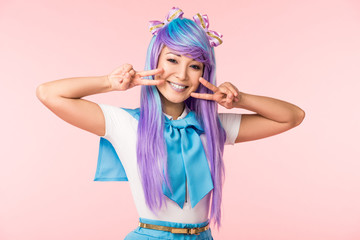 Joyful asian anime girl in purple wig showing peace signs isolated on pink