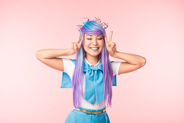 Happy anime girl in purple wig showing peace signs with closed eyes on pink